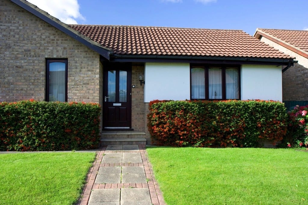 Brick bungalow with tiled roof, dark front door and clipped hedges before AI exterior redesign