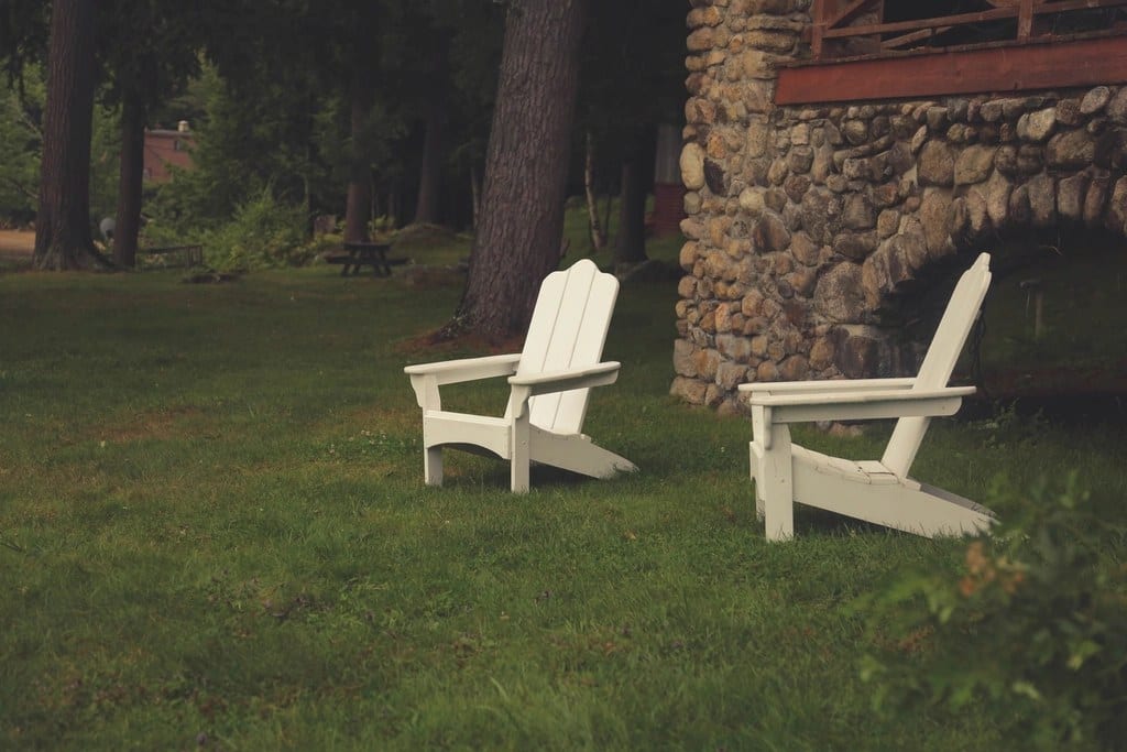 Two white lawn chairs on a plain lawn beside a stone building before AI garden design