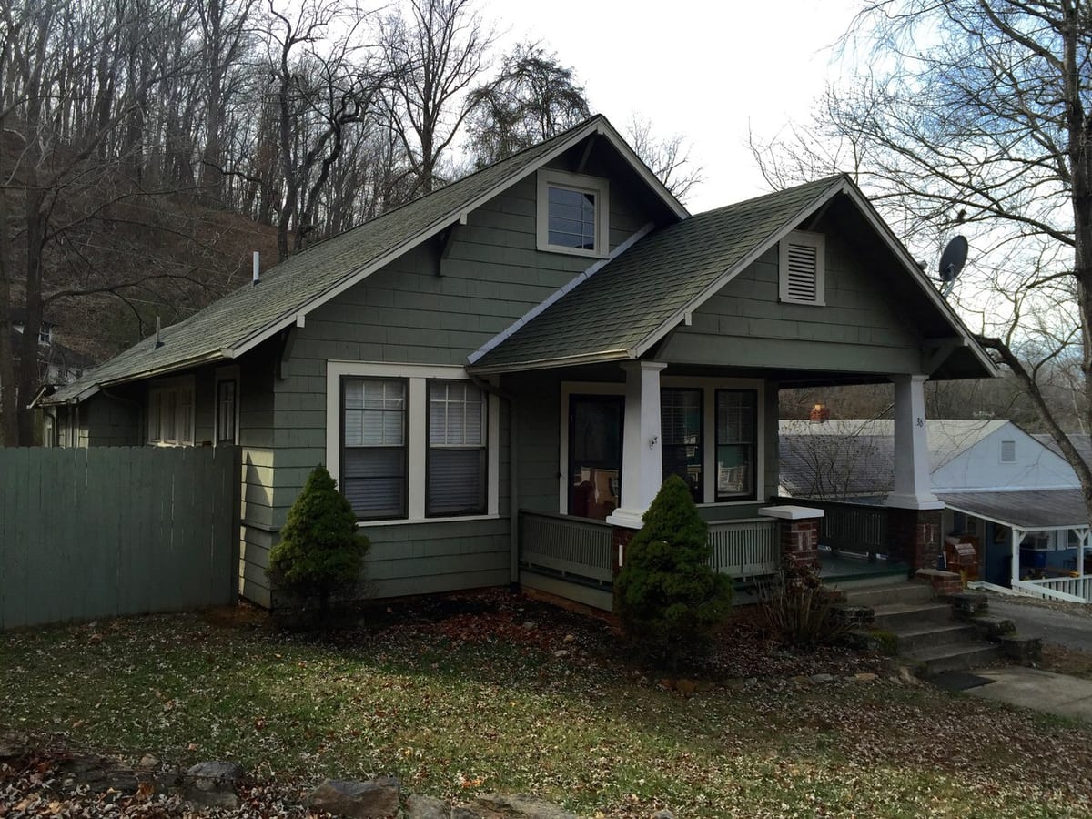 Green Craftsman bungalow with front porch and bare winter yard before AI exterior redesign