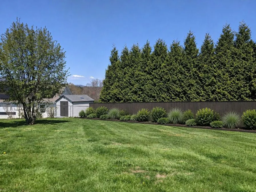 The same backyard as an AI concept with a dark fence and a planted border along it