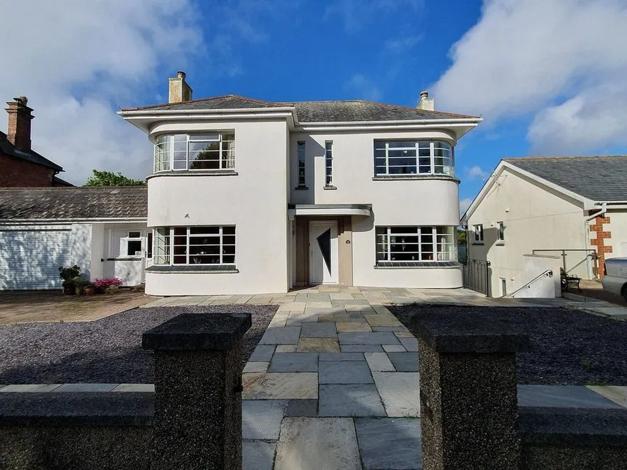 A white stucco house with curved bay windows and a stone paved path between dark gate piers