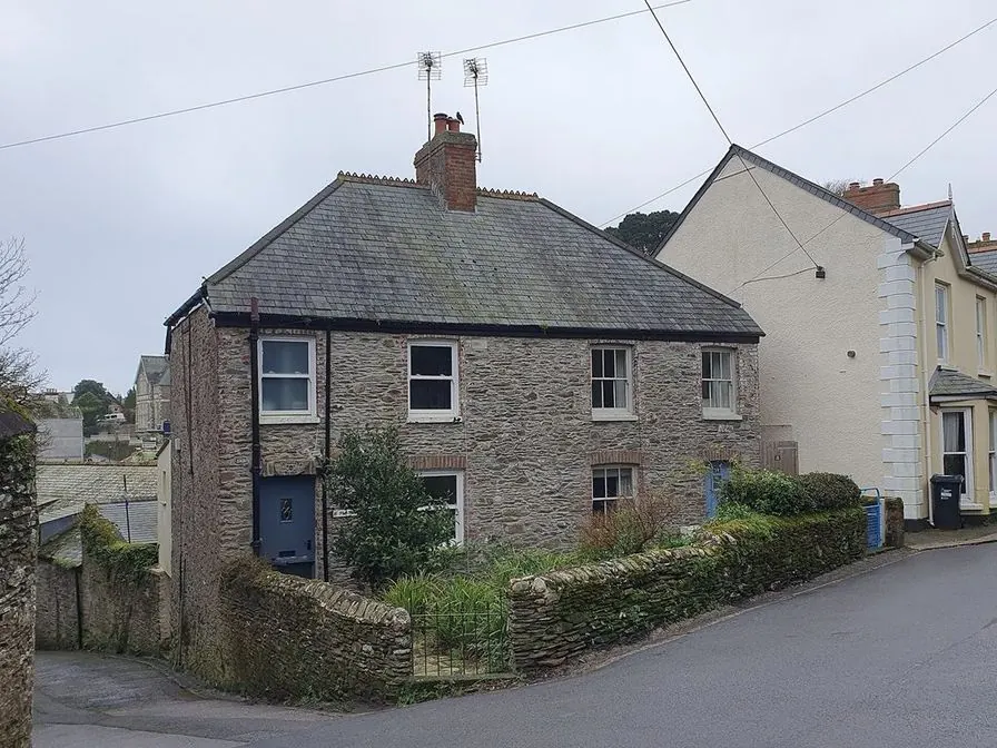 A pair of attached stone houses with a slate roof, a blue door and a hedge