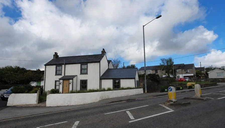 The same house as an AI concept with white board-and-batten walls, black frames and an oak front door