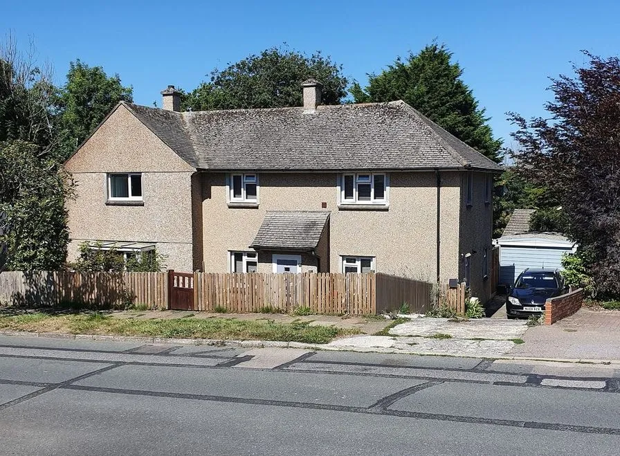 A stucco pair of attached houses with a tiled roof behind a wood fence on a sunny street