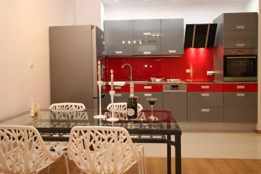 A built-in kitchen with gray cabinets, a red glass backsplash and a dining table