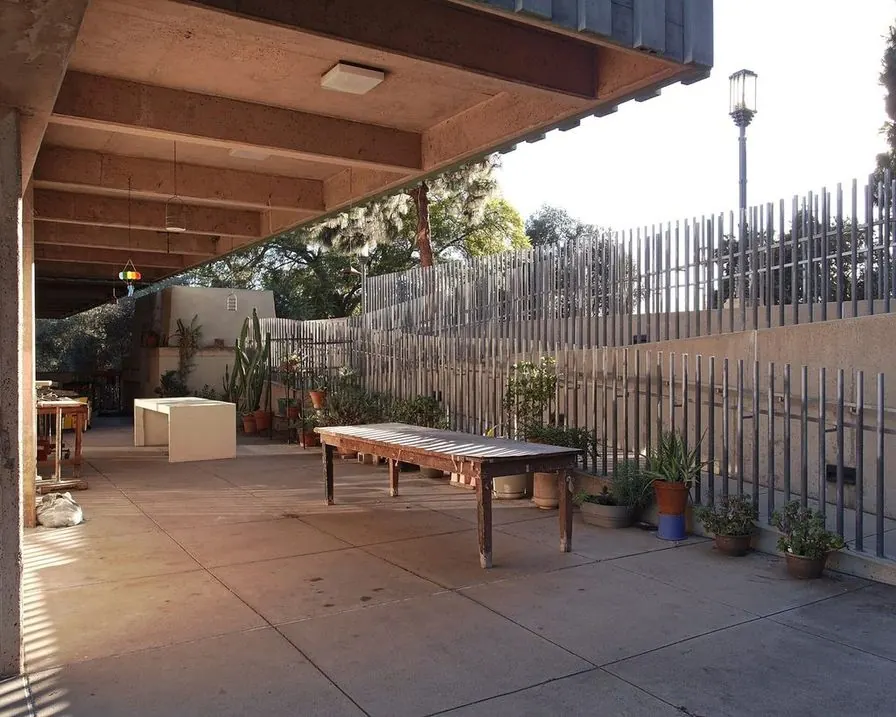 A concrete patio under a covered timber roof with a long table and potted plants