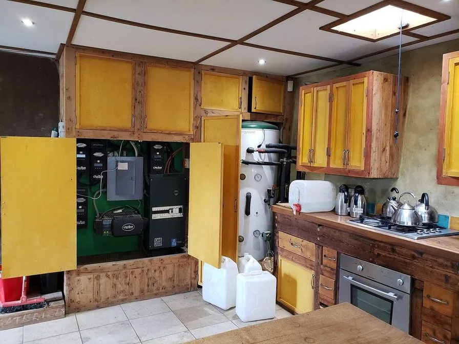 A rustic kitchen with yellow cabinet doors in reclaimed wood frames, an open utility closet and a gas cooktop